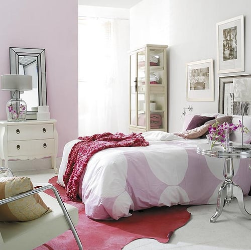 A pink bedroom with purple bedding and a vibrant red leather cowhide rug. 