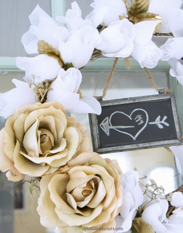 A close up look at a DIY rose wreath with Dollar Tree flowers in white and gold with a small chalkboard sign hanging from the middle. 
