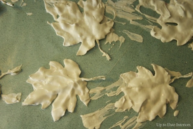 Plaster dipped leaves are drying on wax paper on a green countertop. 