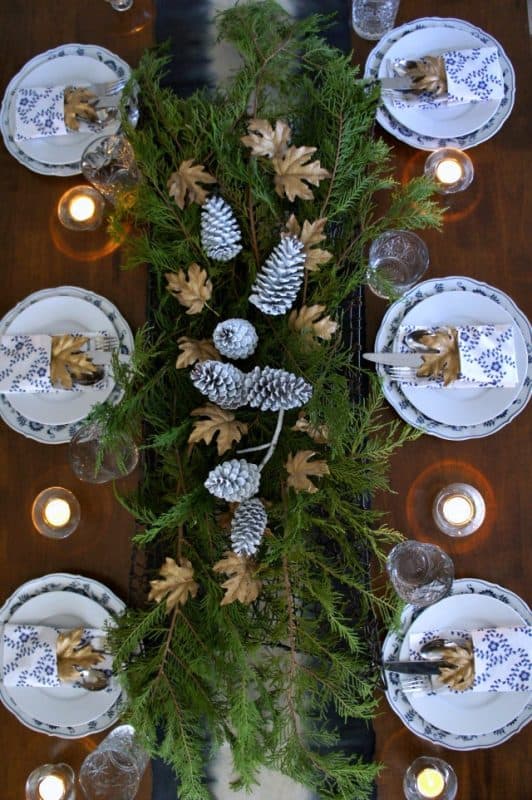 Fresh evergreen sprigs make a garland table centerpiece with blue and white accents. 