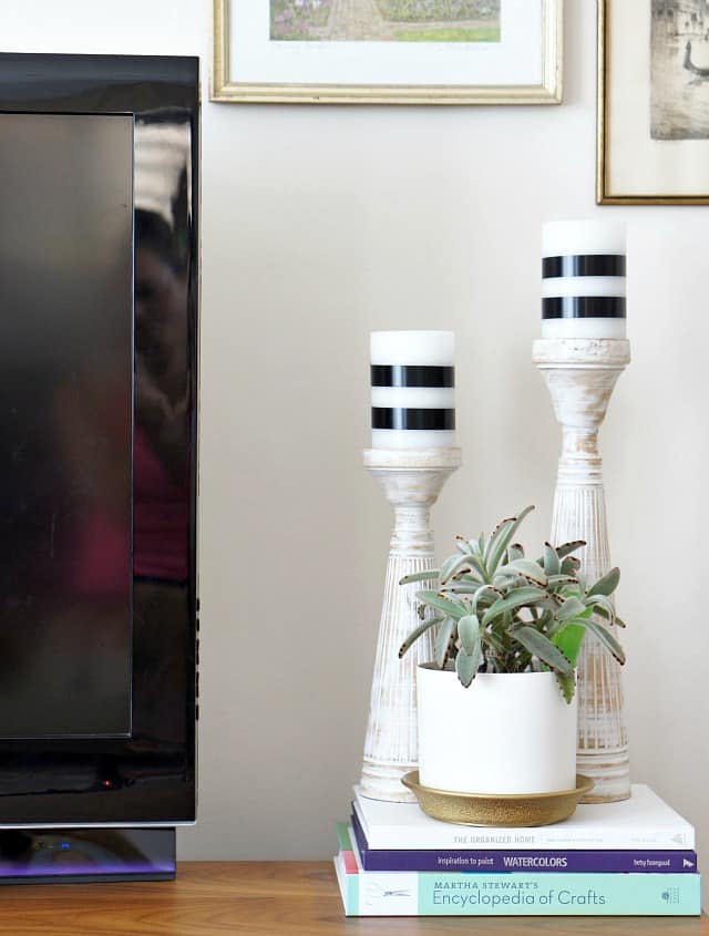 White candles wrapped with black washi tape, plant, books, next to tv. 