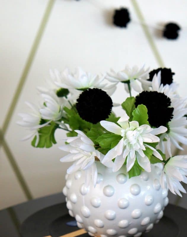 Black pom pom flowers with white flowers in a white vase. 