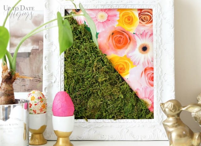 Bright and colorful moss wall decor with moss and floral print in a white frame with a plant, easter eggs, and brass bunny. 