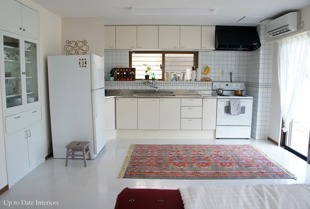 A rental kitchen in Japan before the One Room Challenge makeover.  IT has cream cabinets, white tiles, white linoleum floors and a cute red rug. 