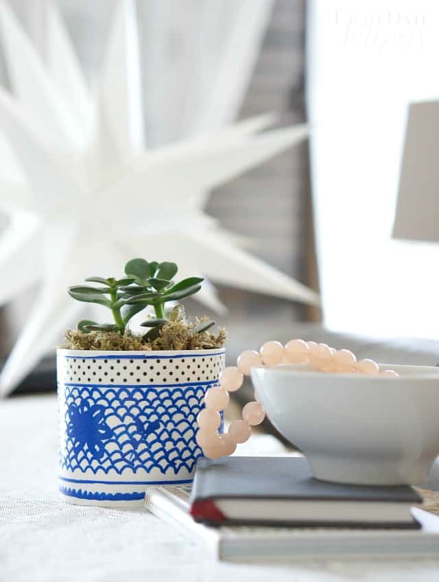 A pottery barn inspired pot diy with blue and white is in a bright and light room with pink beads and small books. 
