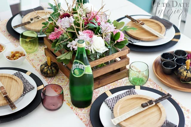 Asian table settings are on a white table with a pink and orange table runner and floral centerpiece in a wooden crate withe beautiful colored tumblers.