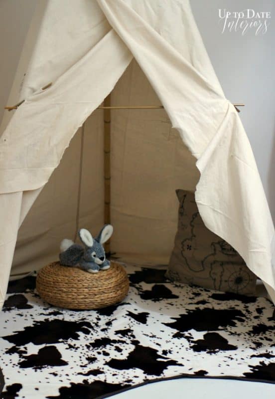 A no-sew teepee with a drop cloth has a faux cowhide rug inside with a basket stool and stuffed bunny. 