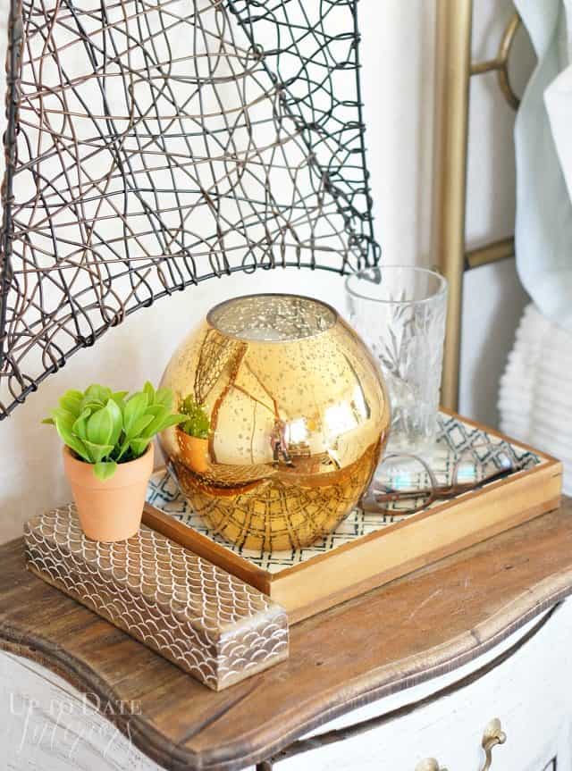 Small bedside table decor featuring global eclectic accessories like a wood scalloped box, Moroccan tray, mercury glass lamp ,and plant. 