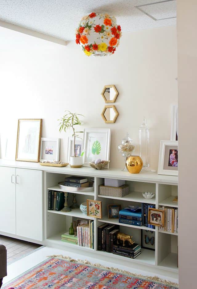 DIY floral paper lantern in a bright white foyer with light mint green built in cabinets and shelves decorated with color coded books and art.  More leaned art lines the counter space. 