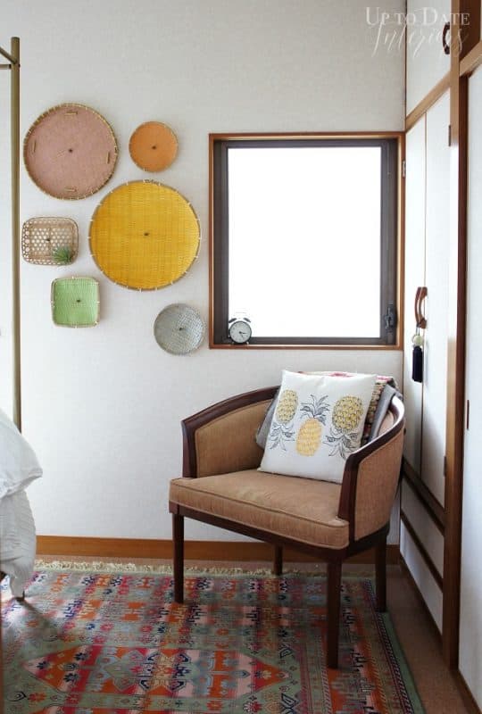 Colorful baskets for global bedroom decor on the wall next to a small window with a tan chair underneath displaying a pineapple pillow.  Cherry diy summer decor for the bedroom! 