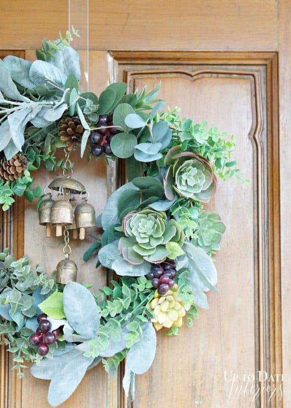 A beautiful succulent wreath hanging on a wood door with brass bells. 
