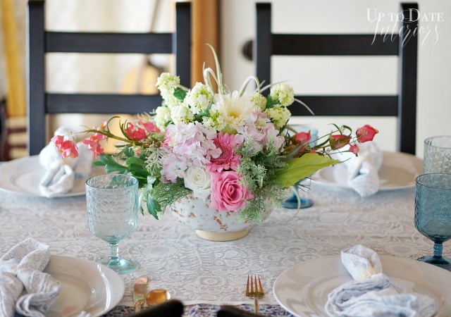 A beautiful and easy flower arrangement centerpiece for spring with pinks and green in a white Japanese pottery bow on a lace table runner with blue and white place settings. 
