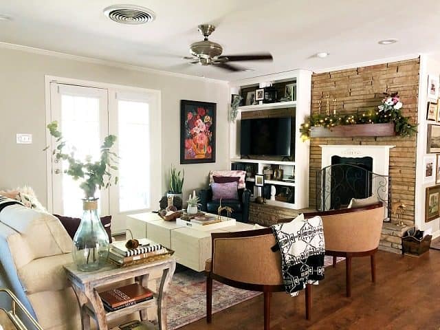 A wide view of an eclectic living room with grey walls, white sofa, tan chairs, white coffee table, lots of layered textiles and decor and fireplace wall. 