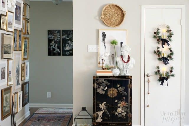 A hallway wall covered in art from floor to ceiling is near a foyer wall with modern global decor and Christmas wreaths hanging on the coat closet. 
