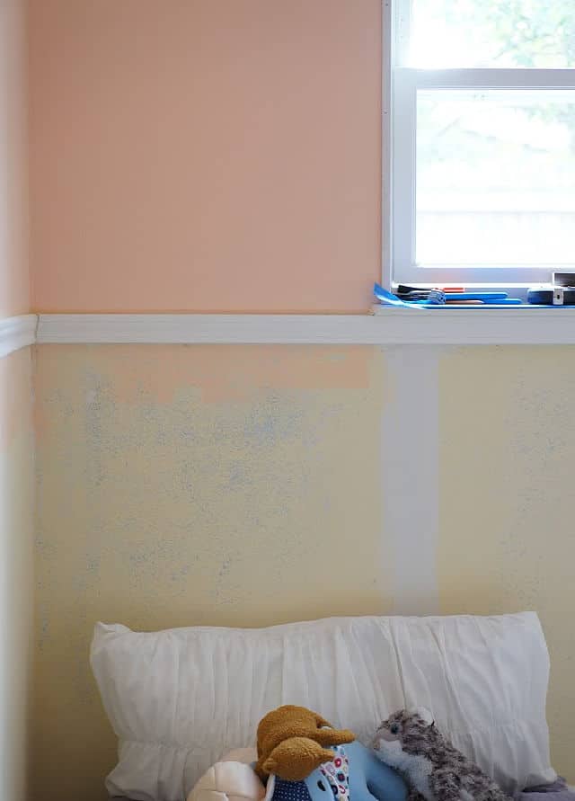 A bedroom wall with chair rail, drywall patching, and window.