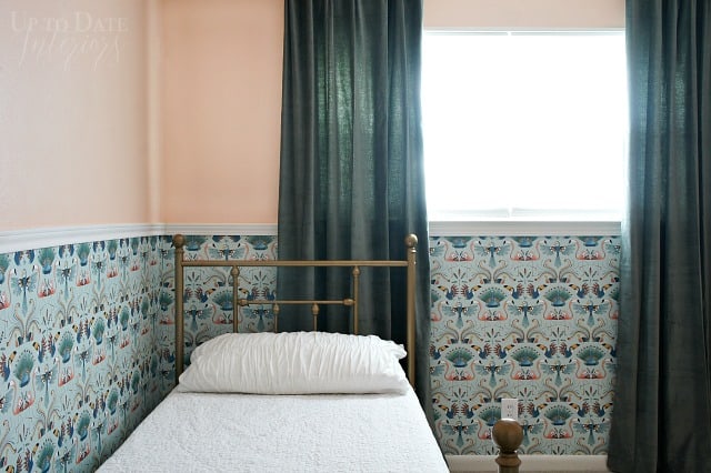 Mint green bird wallpaper lower half of the wall, below a chair rail in a girl's bedroom with pink upper walls, brass twin bed, and green velvet curtains. 