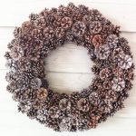 A beautiful and natural pinecone wreath hanging on light wood siding.