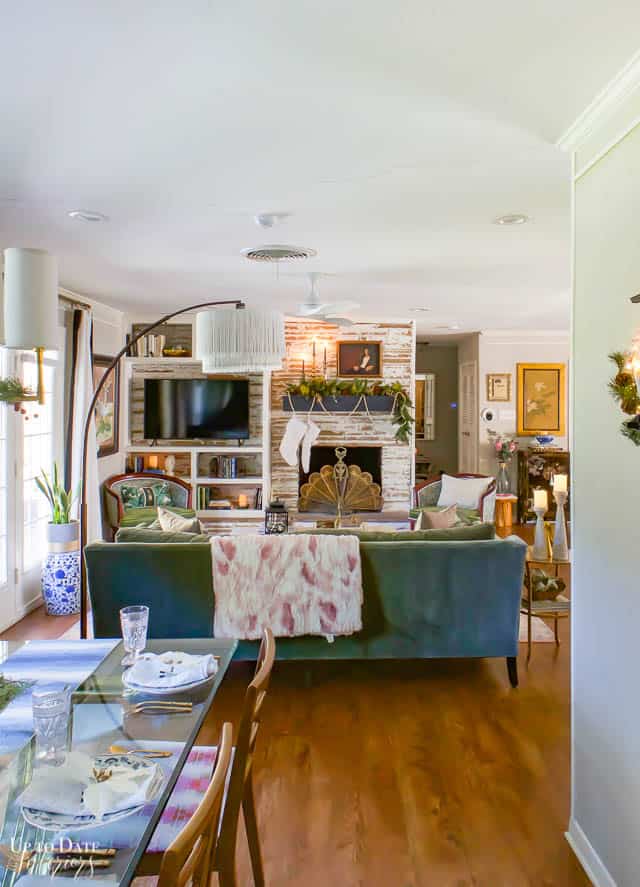 Christmas home tour with elegant decorating ideas.  View from dining are with a glass top table and wood chairs to the back of green velvet couch and german smear fireplace wall.  Lots of eclectic decor. 