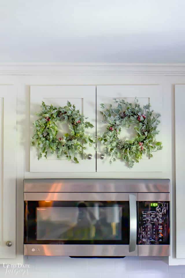 A close up of two wreaths hanging on cabinet doors above the microwave in the kitchen. 