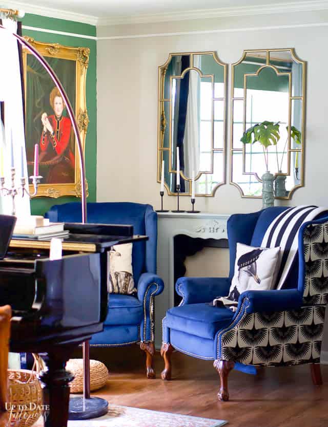 A pair of painted gold mirros above a blue shelf/mantel and two wing back dark blue velvet chairs wtih black adn white accents are cozy and elegant for winter home decor after Christmas.