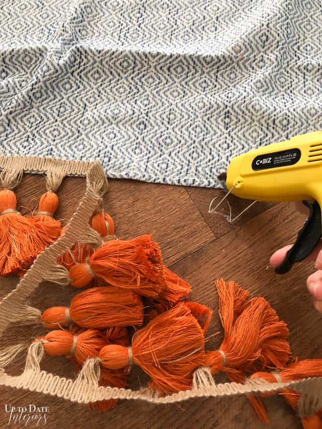 Orange trimming for curtains is being hot glued onto a blue curtain/drapery. 