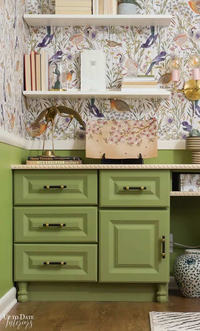 A beautiful maximalist office with green desk cabinets and bird wallpaper.