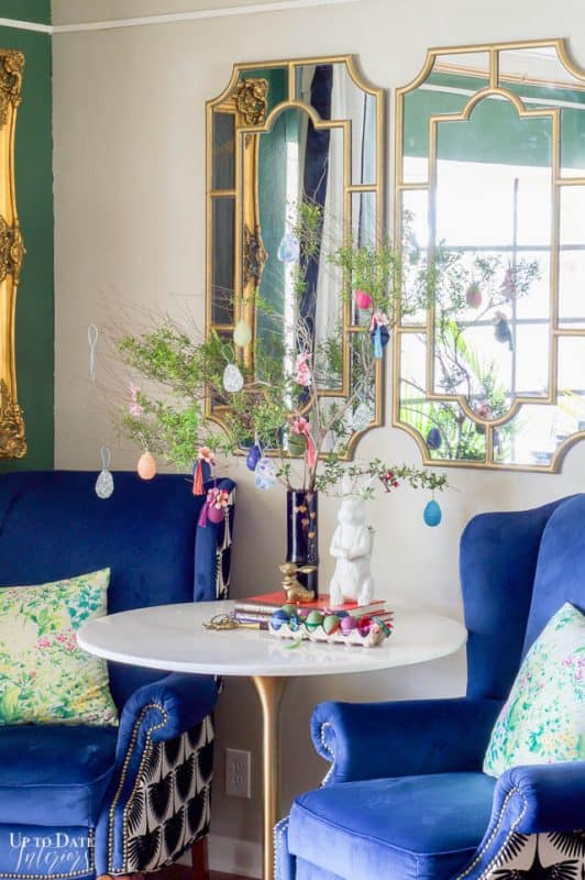 An easter tree with DIY egg ornaments in front of gold mirrors and two blue chairs.