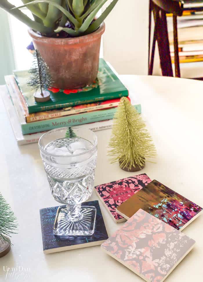 A crystal goblet sits on a DIY decoupage tile coaster with other coasters and books. 