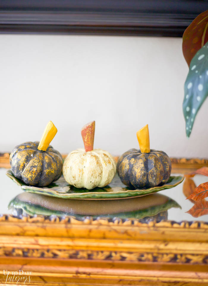 Three wooden Japanese pumpkins on a leaf shaped plate sitting on mirrored cabinet top with gold paint