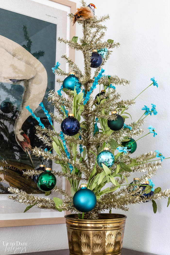 Blue and green Christmas decor in the bedroom with a tinsel tree on a dresser. 