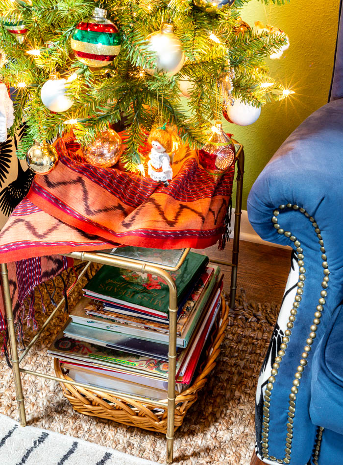 A basket with Christmas books is under a small glass and brass bamboo table. 