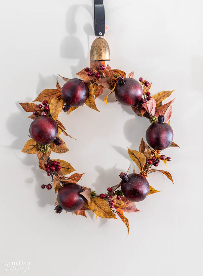 DIY fall wreath with fall leaves, pomegrantes and berries hangs on a white door. 