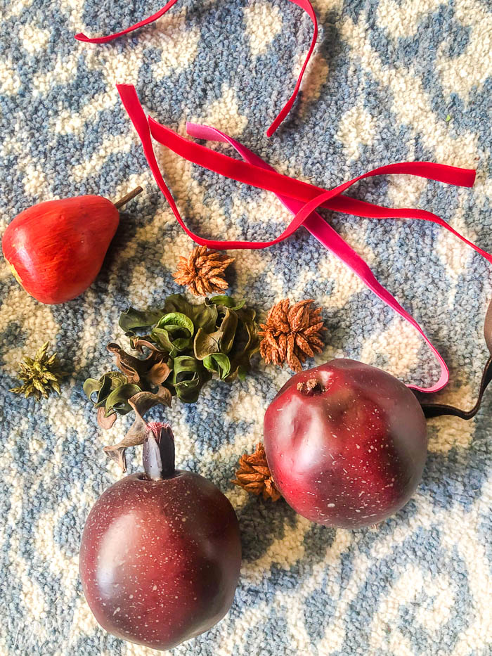 A birds eye view of faux pomegranates and potpourri with a wooden pear and red velvet ribbon laying on a blue and white rug. 