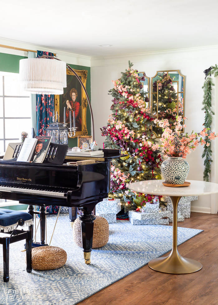 A gorgeous floral Christmas tree sits behind a grand piano with a blue and white large area rug. 