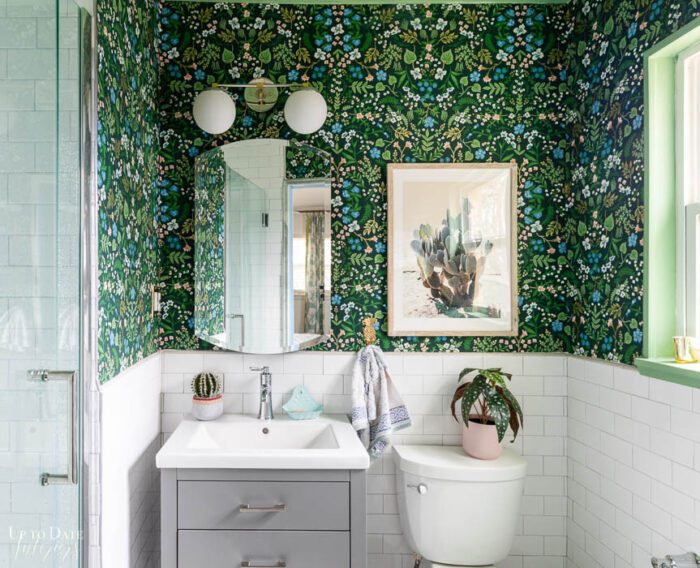 Mixing chrome and brushed nickel finishes in bathroom with grey vanity, white tile, and green floral wallpaper.